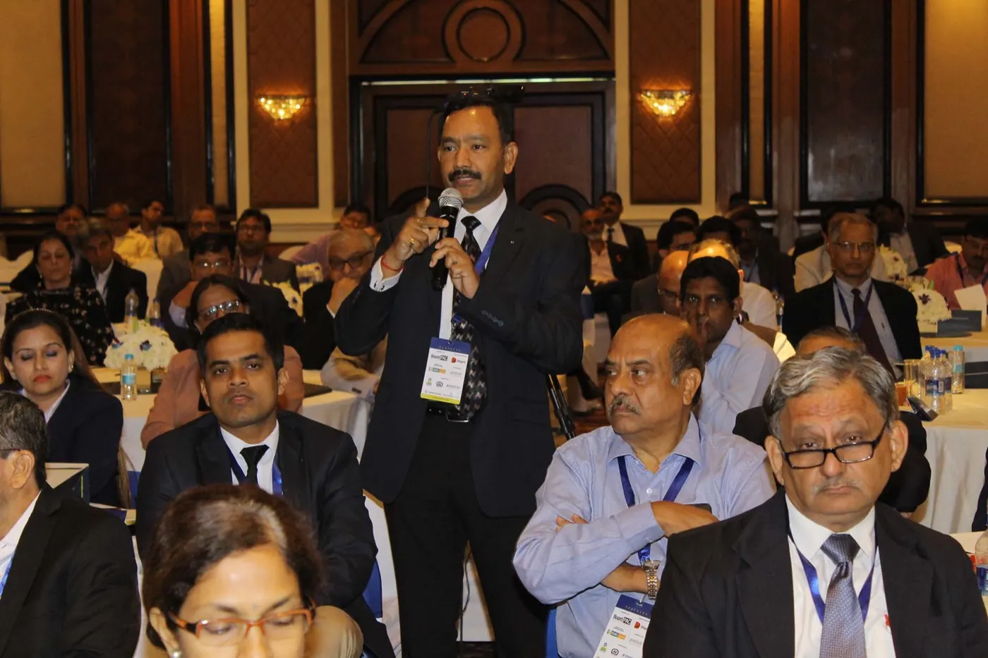 Sudhakar speaking from the floor at a conference, wearing a delegate badge