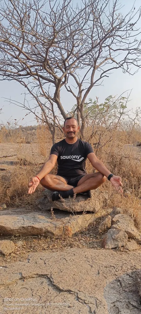 Sudhakar seated cross-legged on rocks, in meditation
