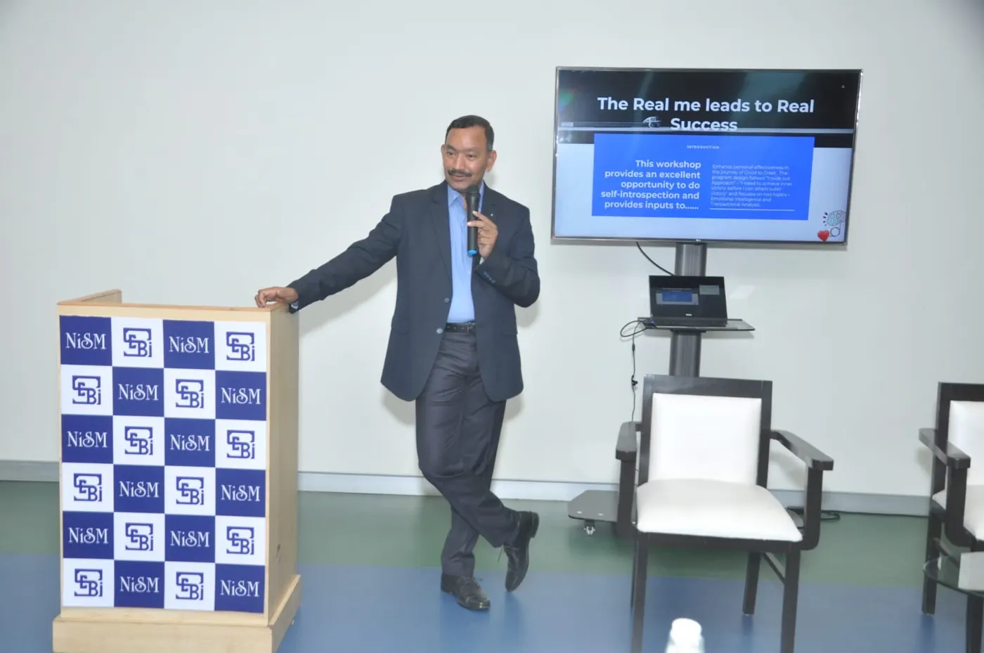 Sudhakar speaking with a microphone beside a slide reading The real me leads to real success